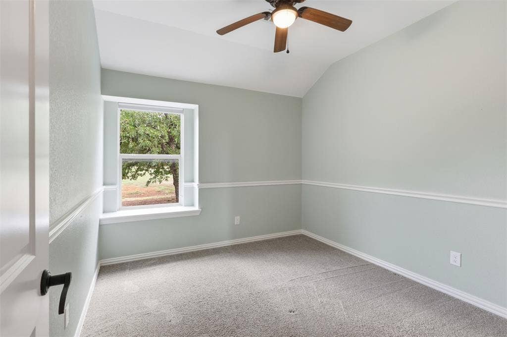 Interior room featuring a vaulted ceiling, neutral wall-to-wall carpeting, decorative chair rail molding, and a built-in ceiling fan with integrated lighting