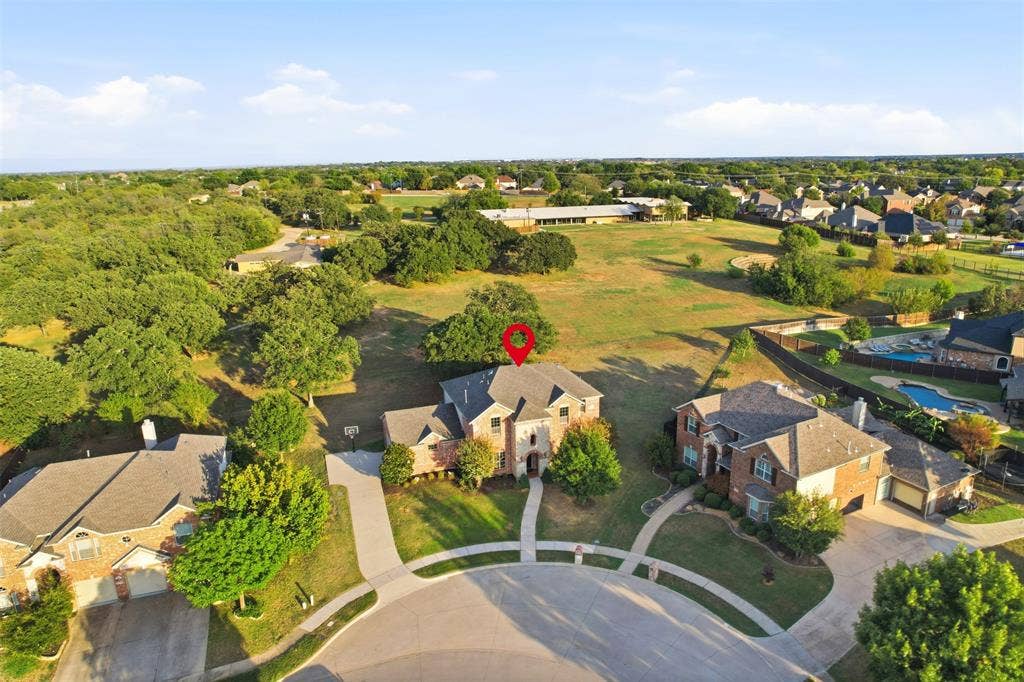 Aerial view of residential property featuring a multi-story brick exterior, attached multi-car garage, concrete driveway, and expansive acreage