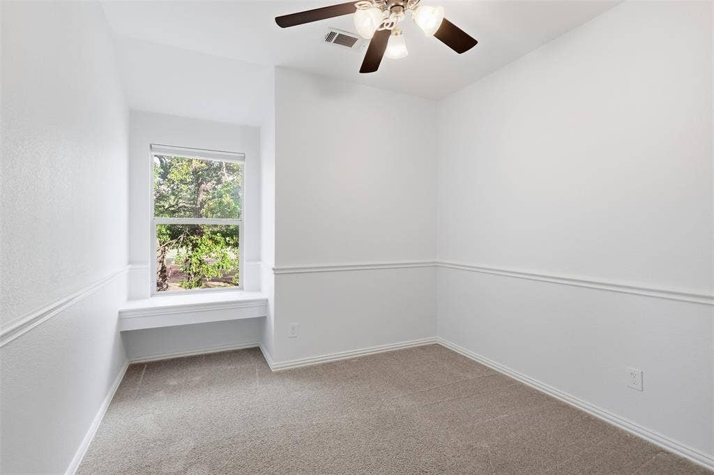 Interior room featuring neutral carpeting, a built-in window seat, chair rail molding, and a ceiling fan with integrated lighting