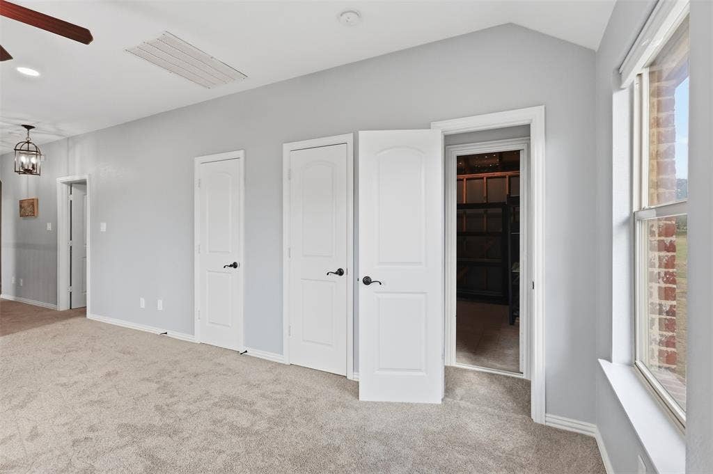 Vaulted ceilings with recessed lighting, neutral carpeting, three-panel interior doors with matte black hardware, and an expansive window with a brick exterior surround