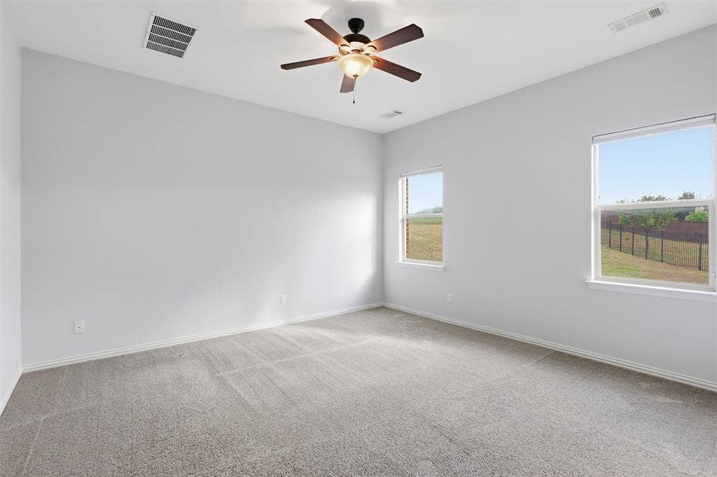 Neutral-toned room featuring neutral carpeting, a multi-blade ceiling fan with integrated lighting, and dual windows