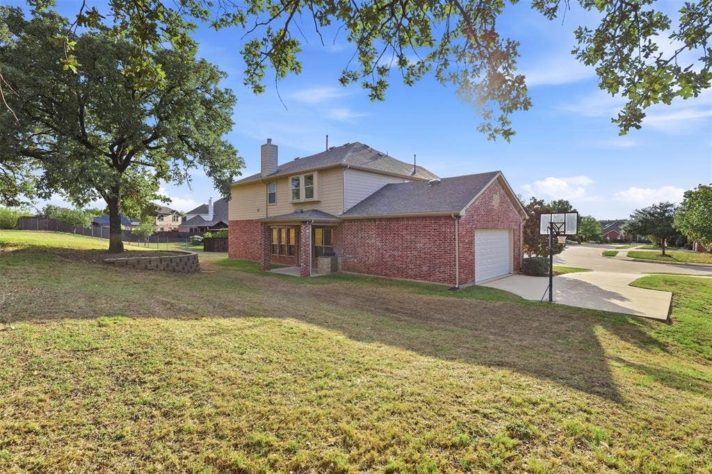 Two-story residence featuring brick and siding exterior, expansive grounds with mature trees, a multi-level retaining wall, and a concrete driveway