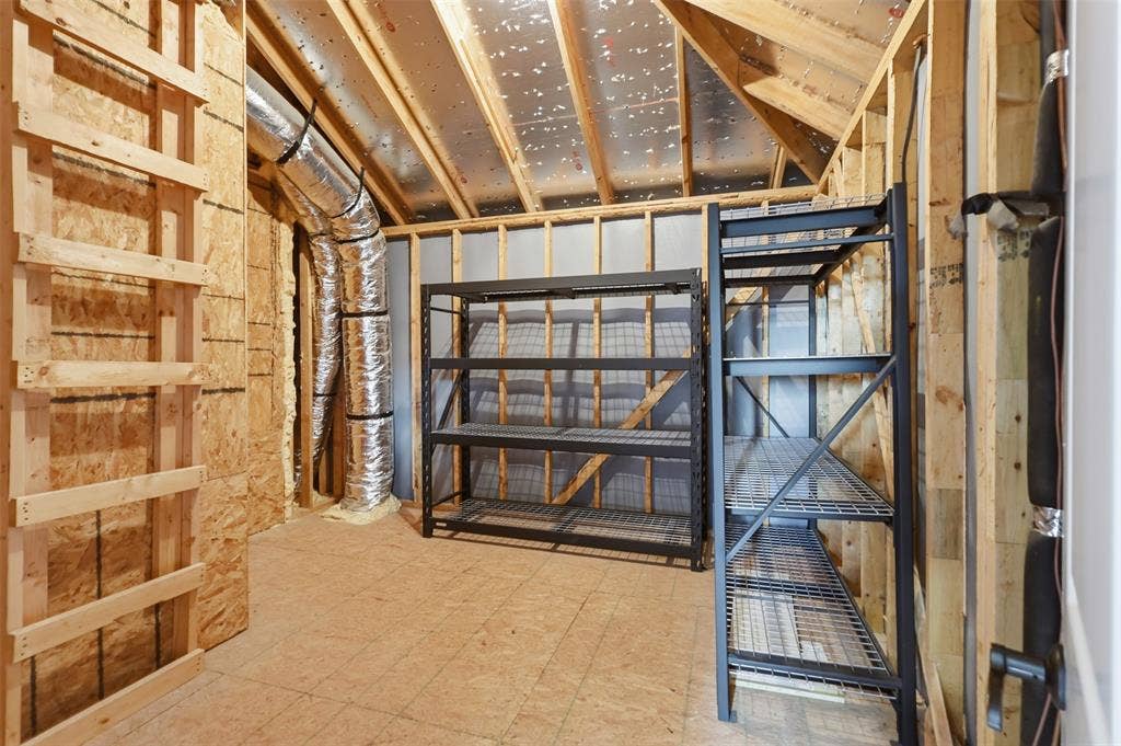 Unfinished storage space featuring exposed wood-stud framing, plywood flooring, and structural ceiling rafters with reflective insulation backing