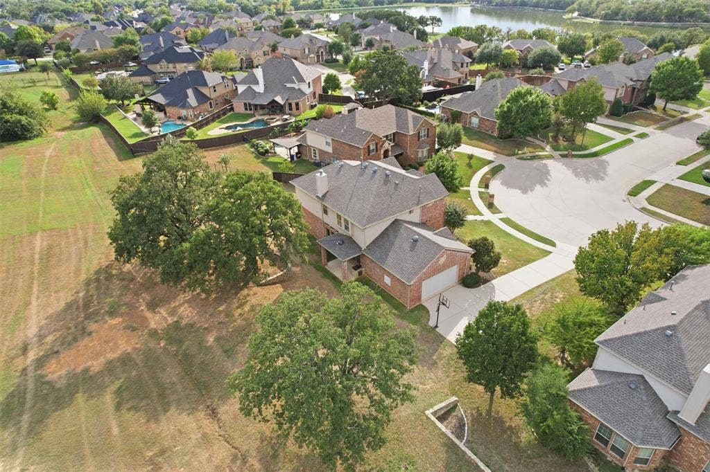 Two-story brick and masonry exterior featuring an attached two-car garage, steep-pitched roof, stone chimney, and expansive corner lot with mature trees