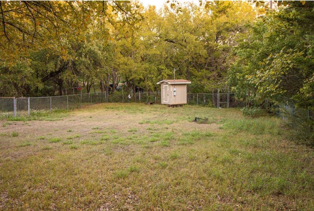 Fenced backyard featuring an expansive lawn, mature trees, and a detached storage structure
