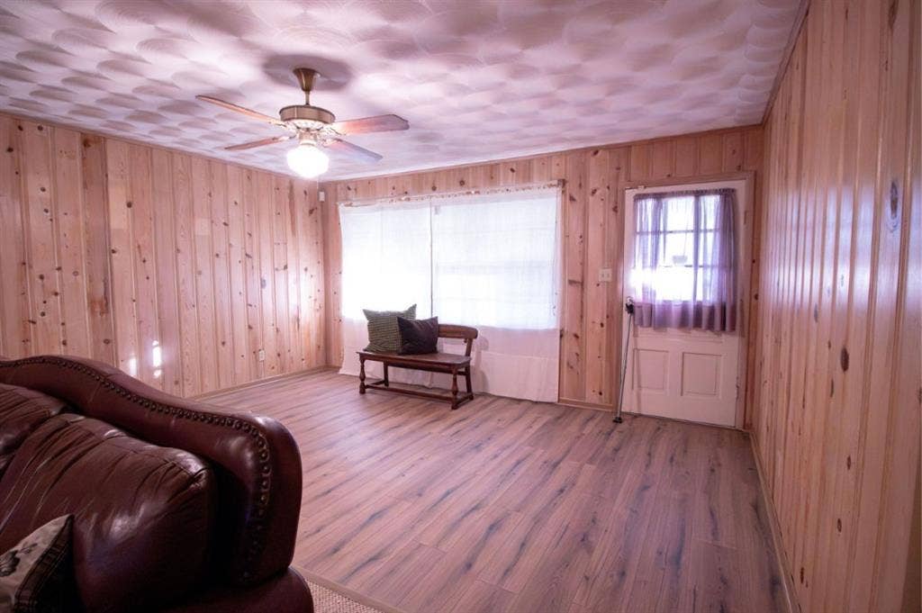 Knotty pine wood wall paneling, wood-finish flooring, ceiling fan with integrated lighting, and a six-panel exterior door with a windowed upper insert