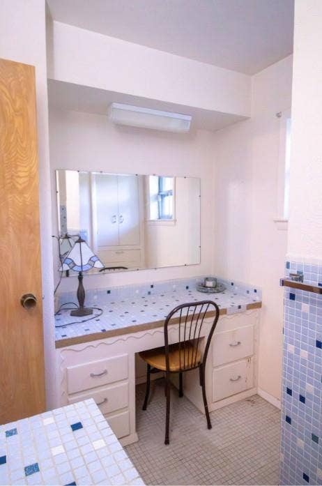 Built-in vanity featuring a tiled countertop, white cabinetry with integrated drawer storage, a wall-mounted rectangular mirror, and blue and white mosaic tile accents