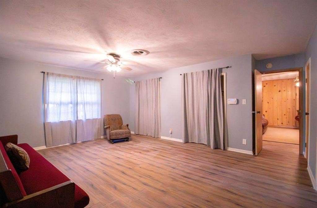Spacious room featuring wood-finish flooring, a ceiling-mounted light fixture with fan, and multiple closets