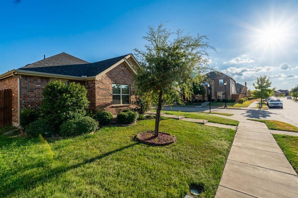 Brick exterior, composition shingle roof, concrete sidewalk, and landscaped front lawn with mature tree