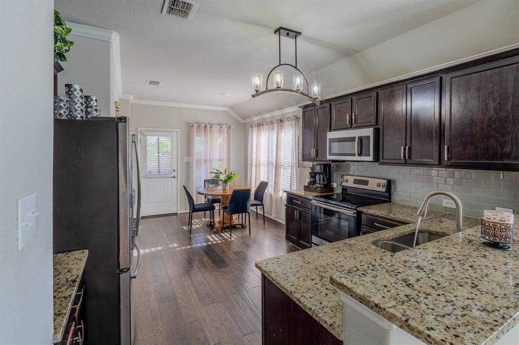 Kitchen featuring dark wood cabinetry, stone countertops, subway tile backsplash, stainless steel appliances, and wood-finish flooring