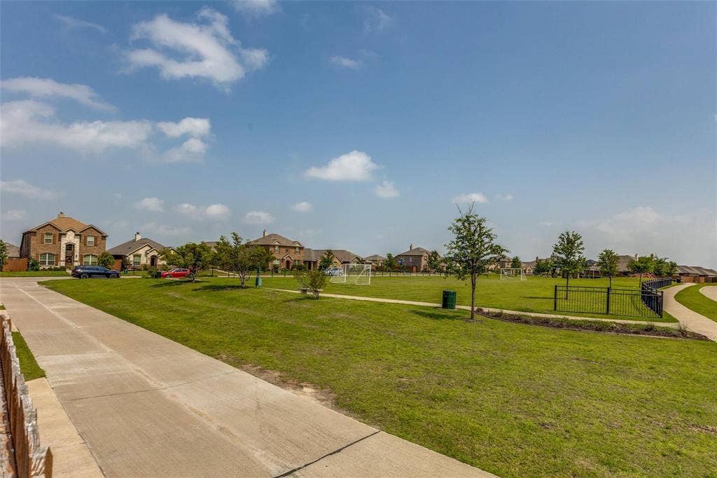 Expansive green space featuring a concrete pathway, mature trees, and metal perimeter fencing