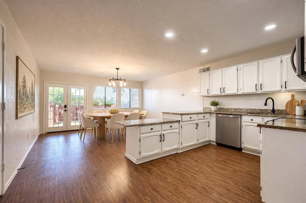 Kitchen featuring white cabinetry, stone-finish countertops, stainless steel dishwasher, wood-finish flooring, and double glass-paneled exterior doors