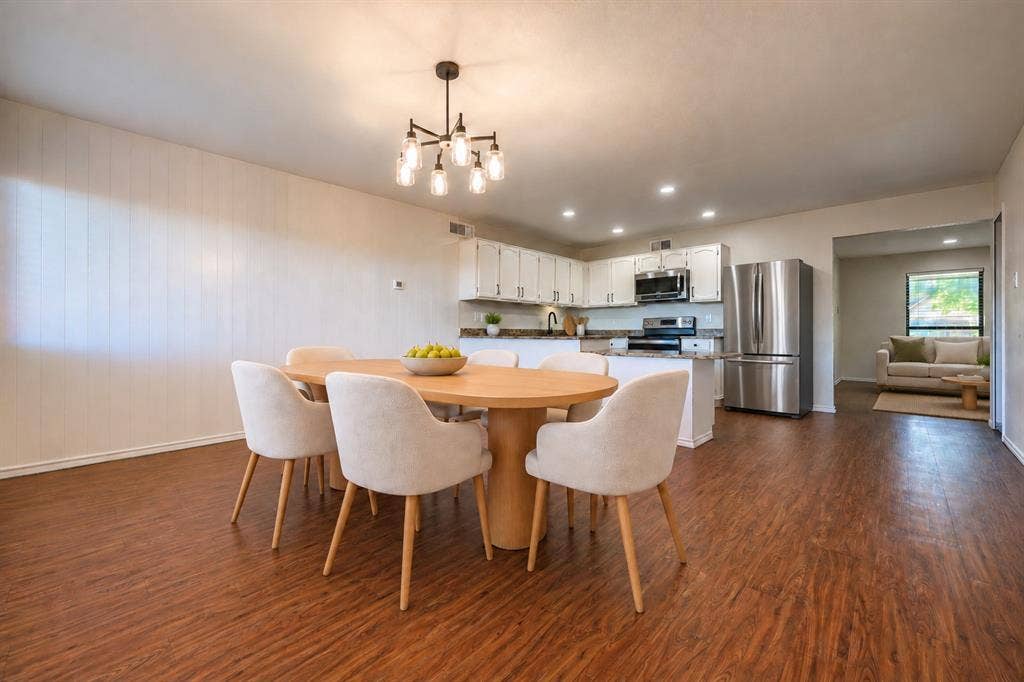 Open-concept kitchen featuring white cabinetry, stainless steel appliances, a multi-arm chandelier, and wood-finish flooring