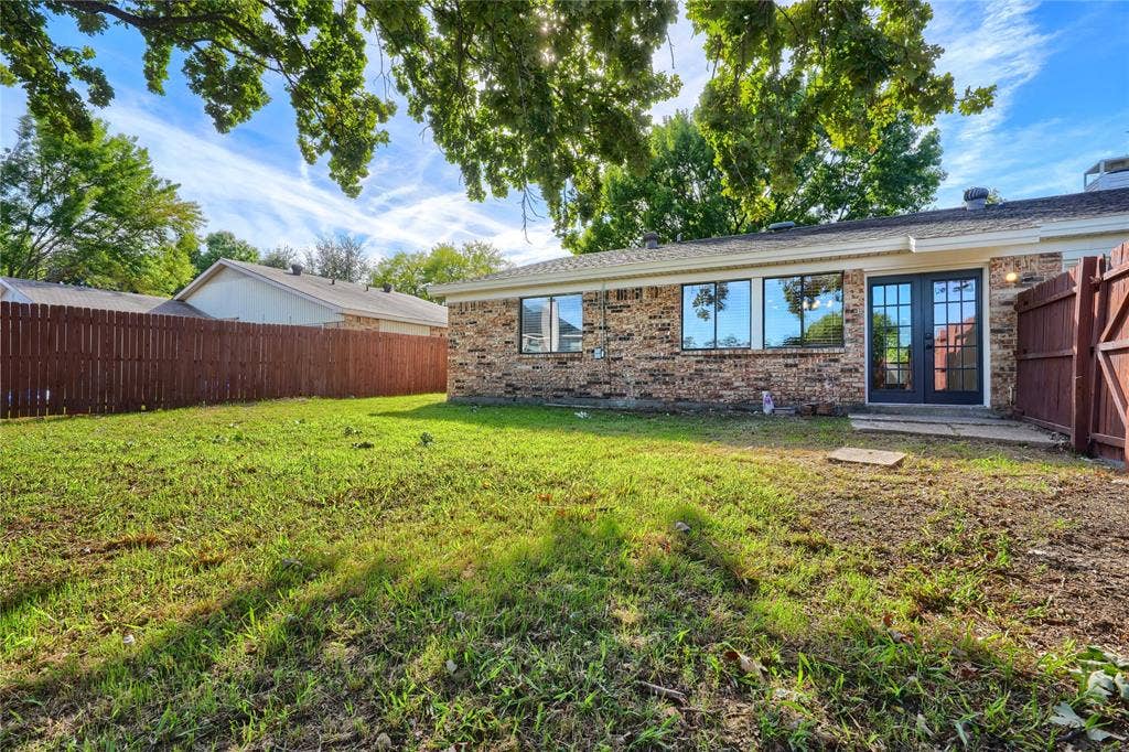 Backyard featuring brick exterior, mature shade trees, full-perimeter wood fencing, and double glass-pane doors