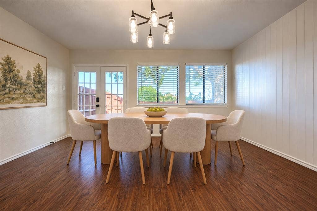 Dining area featuring wood-finish flooring, vertical shiplap accent wall, six-light chandelier with glass pendants, and a full-light glass panel door
