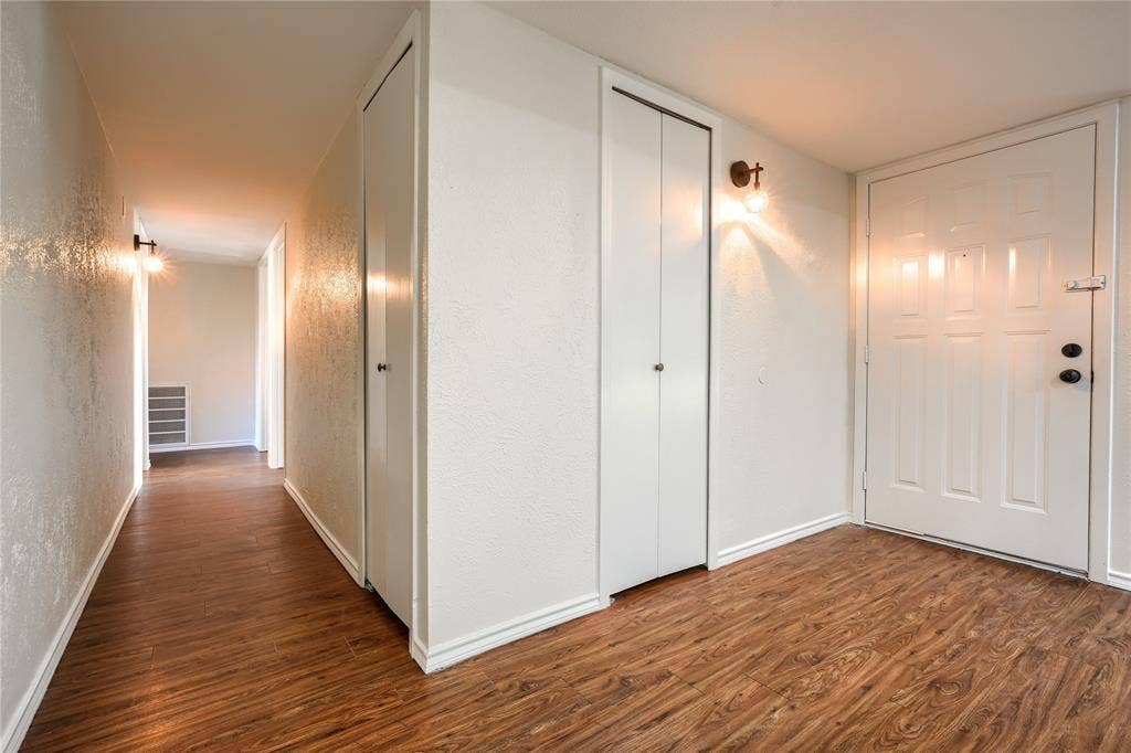 Wood-finish flooring, white paneled entry door with deadbolt, dual bi-fold closets, and wall-mounted sconce lighting