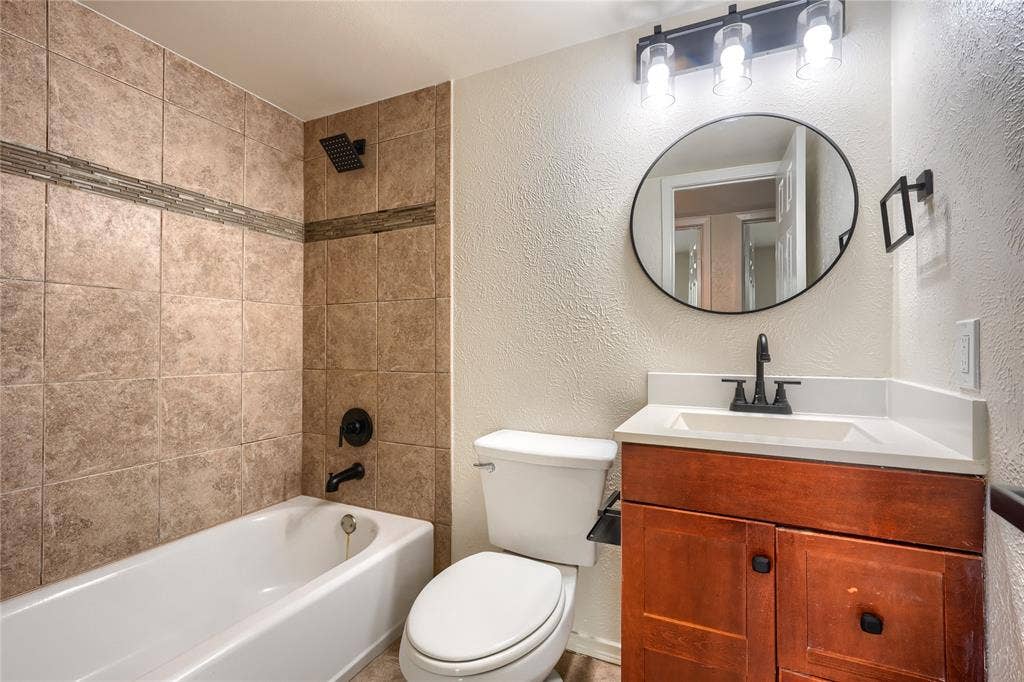 Bathroom featuring a wood-finish vanity with a white countertop, oval wall-mounted mirror, matte black plumbing fixtures, and a shower-tub combination with tile surround