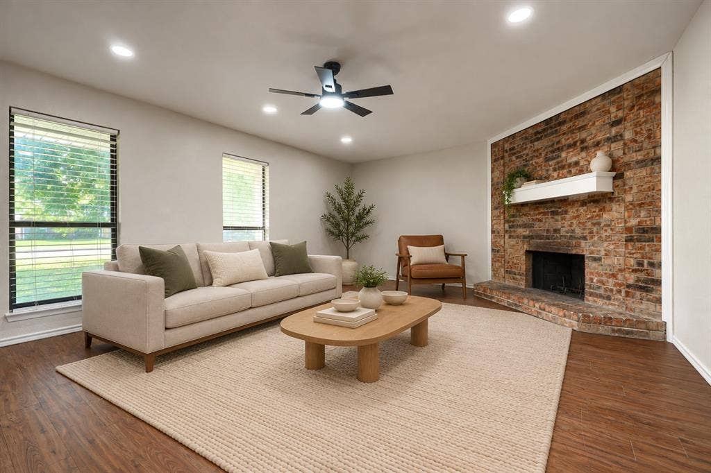 Living area featuring wood-finish flooring, recessed lighting, a ceiling fan with integrated lighting, two windows, and an exposed brick fireplace with a built-in mantle