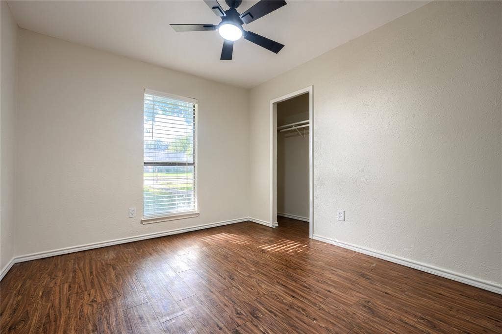 Interior space featuring wood-finish flooring, a neutral wall palette, a single-hung window, a ceiling-mounted light fixture with a fan, and a built-in closet with a shelf and clothing rod