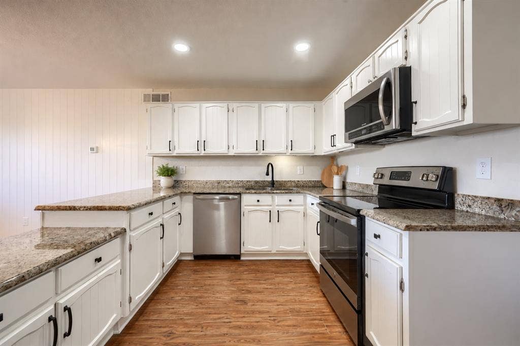 Kitchen featuring white cabinetry, stone-finish countertops, stainless steel appliances, a matte black faucet, and wood-finish flooring