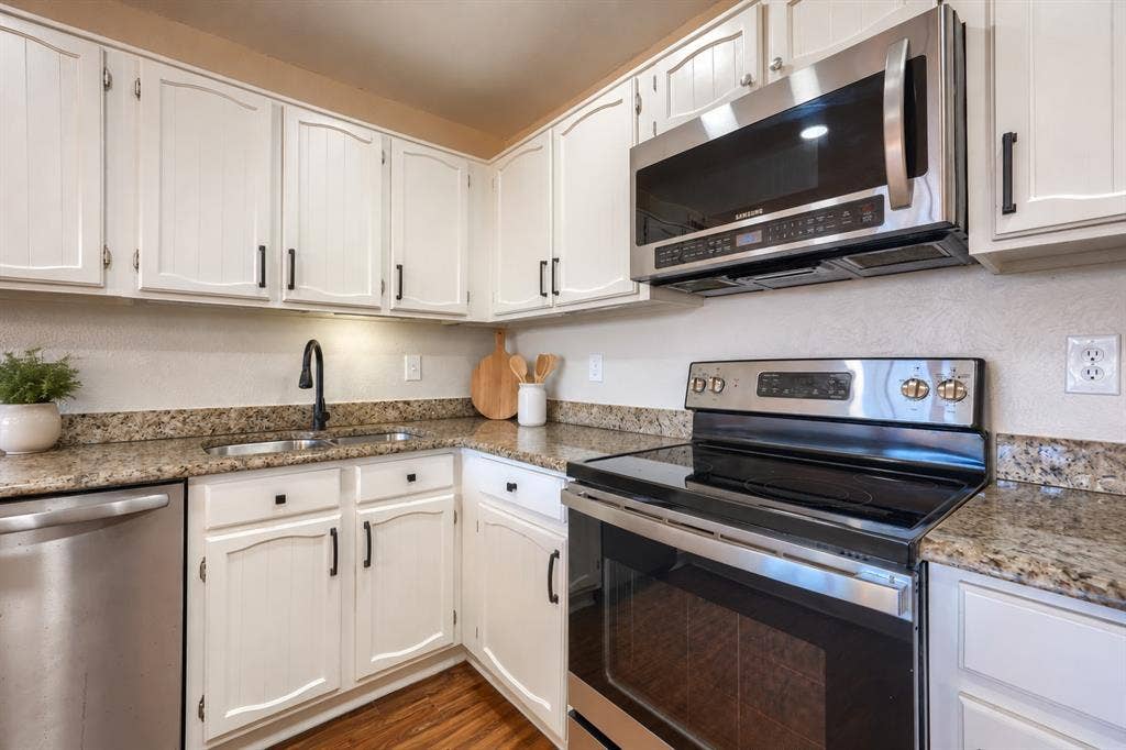Kitchen featuring white cabinetry, stainless steel appliances, speckled stone countertops, matte black hardware, and wood-finish flooring