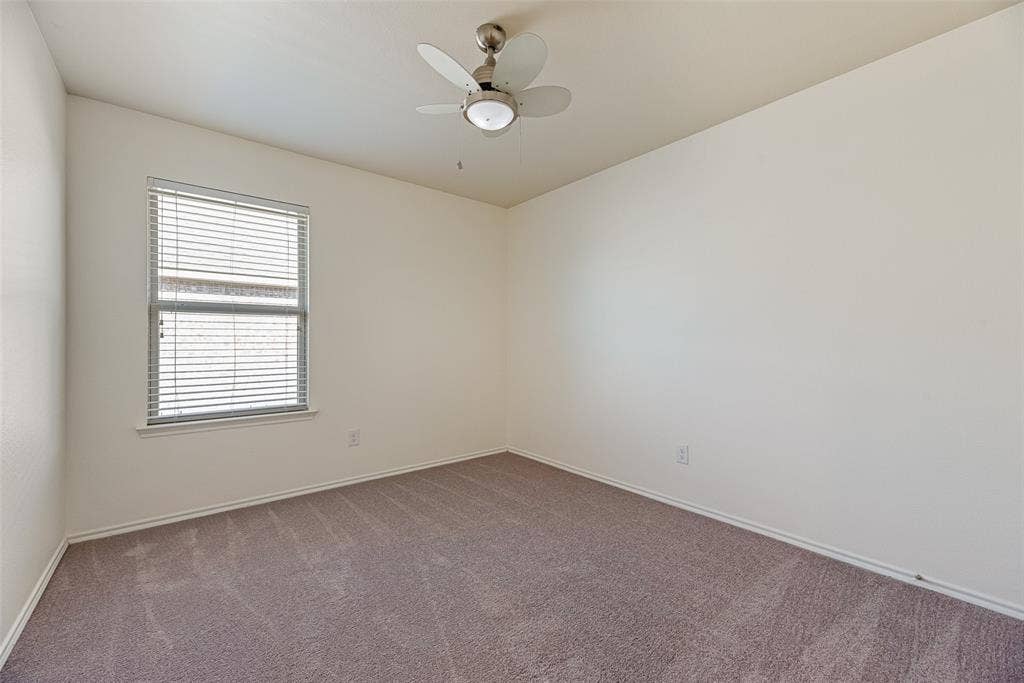 Neutral-toned carpeted flooring, window with installed horizontal blinds, and a multi-blade ceiling fan with integrated light fixture