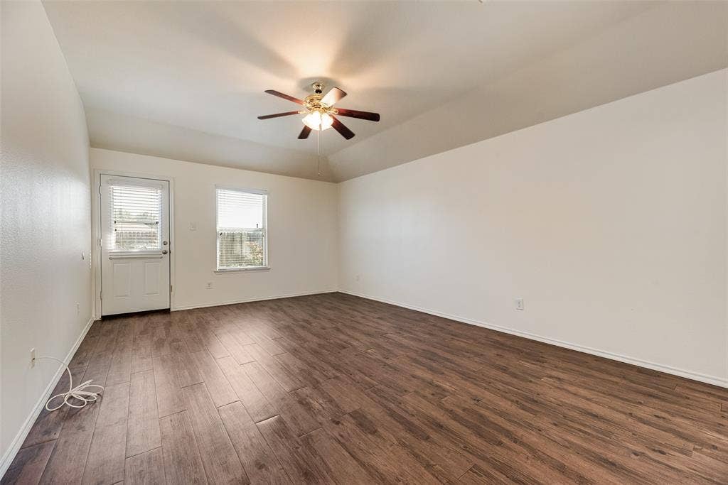 Vaulted ceilings featuring a centrally mounted ceiling fan with integrated lighting, wood-finish flooring, and natural light provided by a single-hung window and glass-panel door