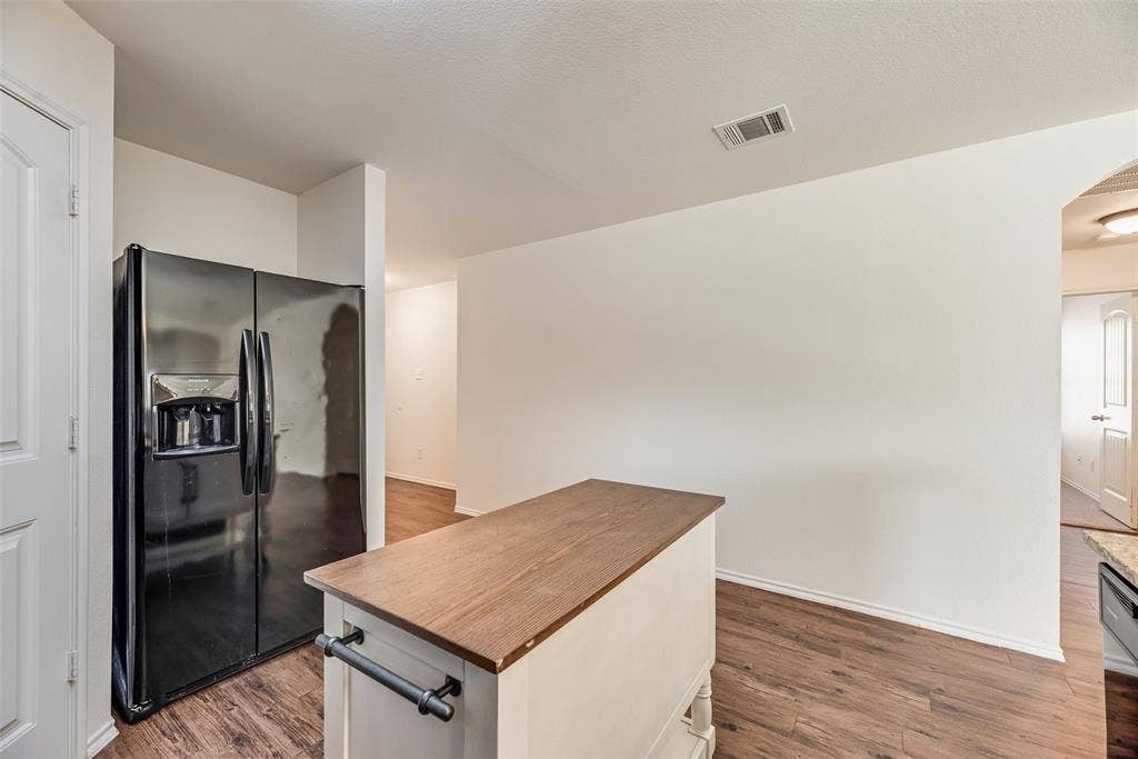 Kitchen interior featuring wood-finish flooring, a matte black side-by-side refrigerator, and a mobile island with a wood-grain countertop and black hardware