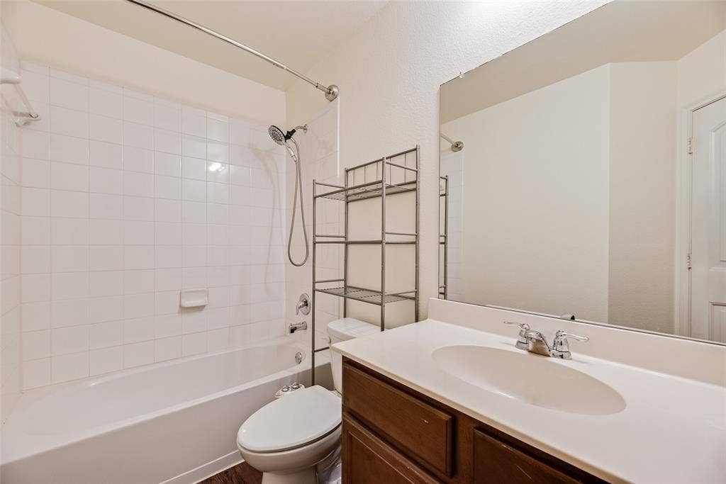 Bathroom featuring a single-sink vanity with a solid-surface countertop, a full-width wall mirror, and a shower-tub combination with white tile surround
