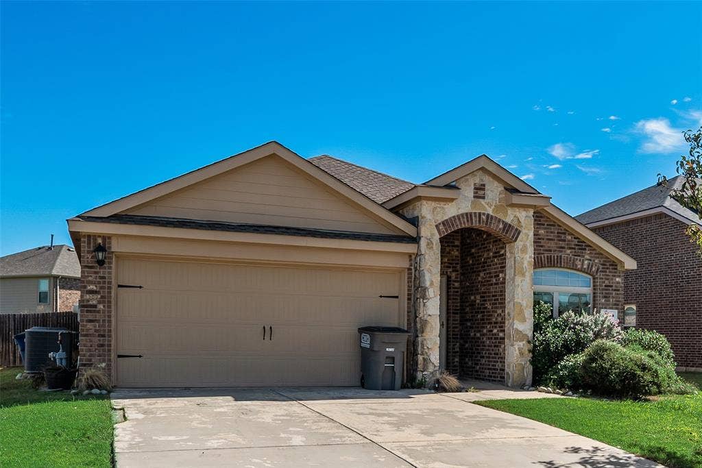 Single-story exterior featuring a brick and stone facade, arched entryway, two-car garage, and concrete driveway