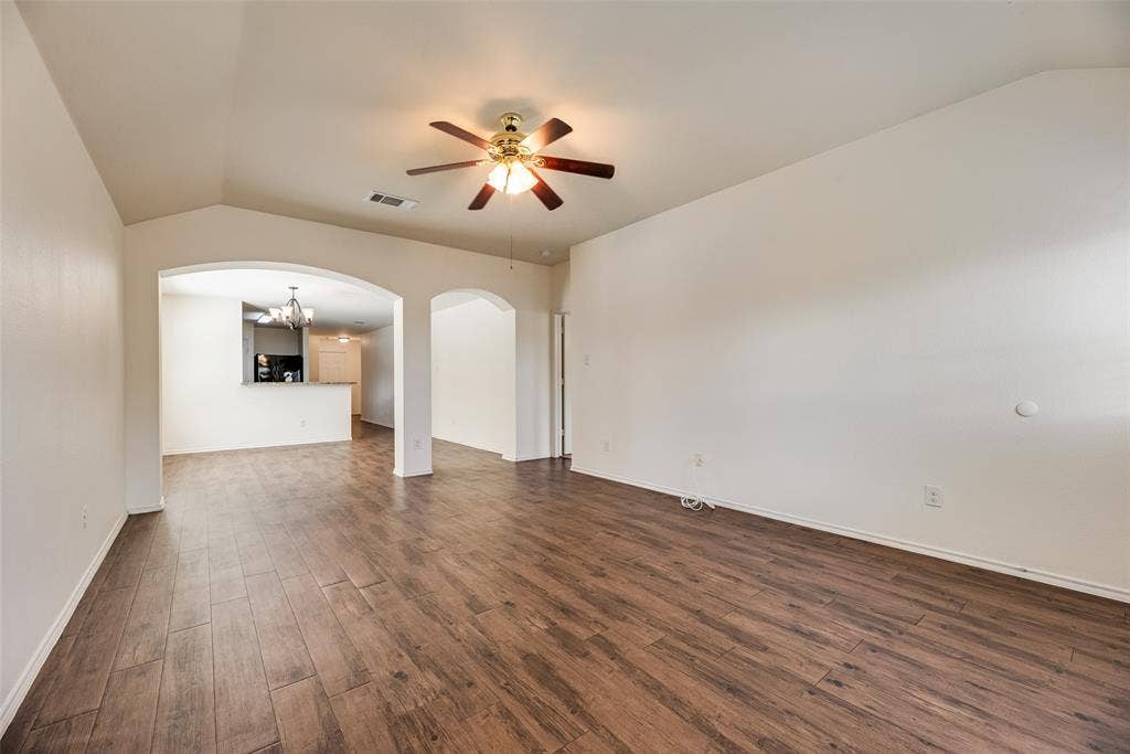 Vaulted ceilings featuring a multi-blade ceiling fan and arched architectural openings finished with wood-finish flooring