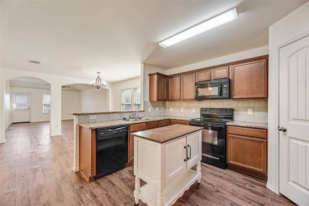 Kitchen featuring wood-finish flooring, stained wood cabinetry, stone-surface countertops, tile backsplash, and built-in appliances