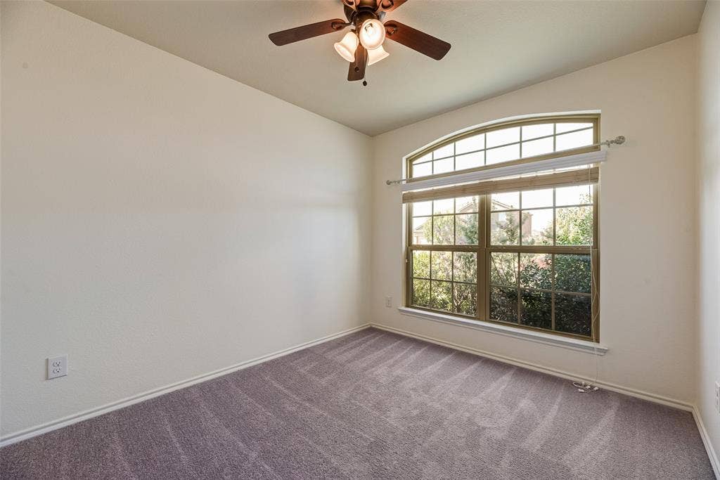 Arched window with grid detailing, neutral carpeting, ceiling fan with integrated lighting, and off-white wall finish