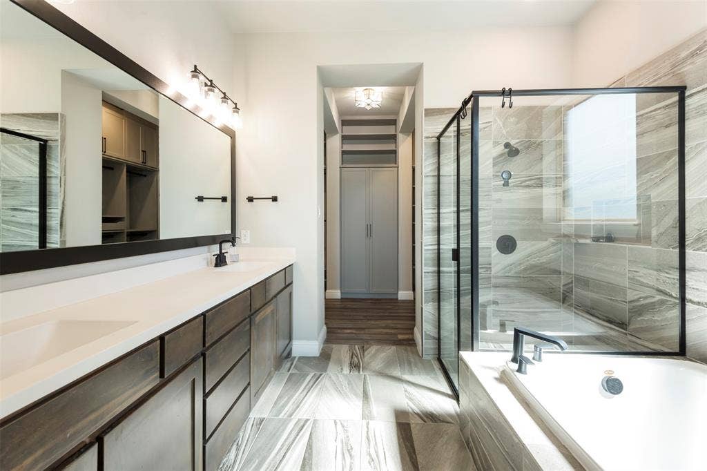 Double vanity with solid-surface countertops, large framed mirror, glass-enclosed shower with tiled surround, built-in cabinetry, and tile flooring
