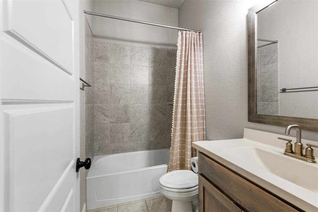 Bathroom featuring a wood-finish vanity with an integrated countertop, metallic faucet, large framed mirror, and a tub-shower combination with full-height tile surround