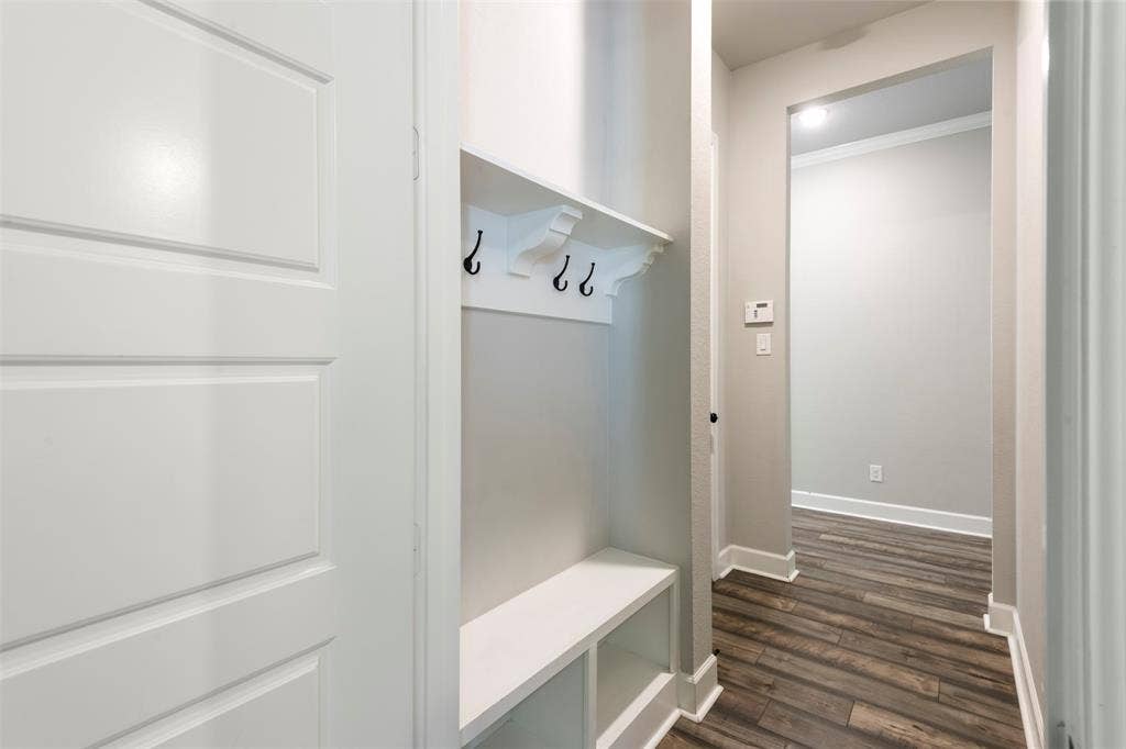 Built-in entryway storage featuring a bench, open shelving, and wall-mounted hooks, complemented by wood-finish flooring and a multi-panel door