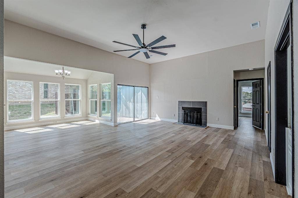 Living area featuring high ceilings, wood-finish flooring, a fireplace with a neutral tile surround, large windows, and a multi-blade ceiling fan