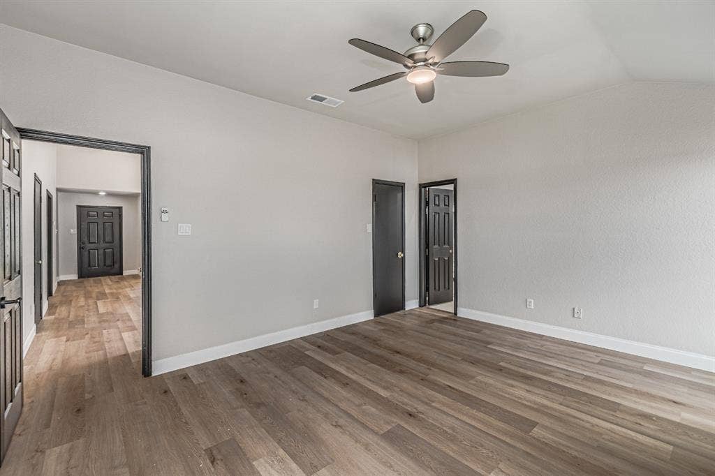 Vaulted ceiling featuring a central brushed-nickel ceiling fan with integrated lighting, complemented by wood-finish flooring and high-contrast dark door frames