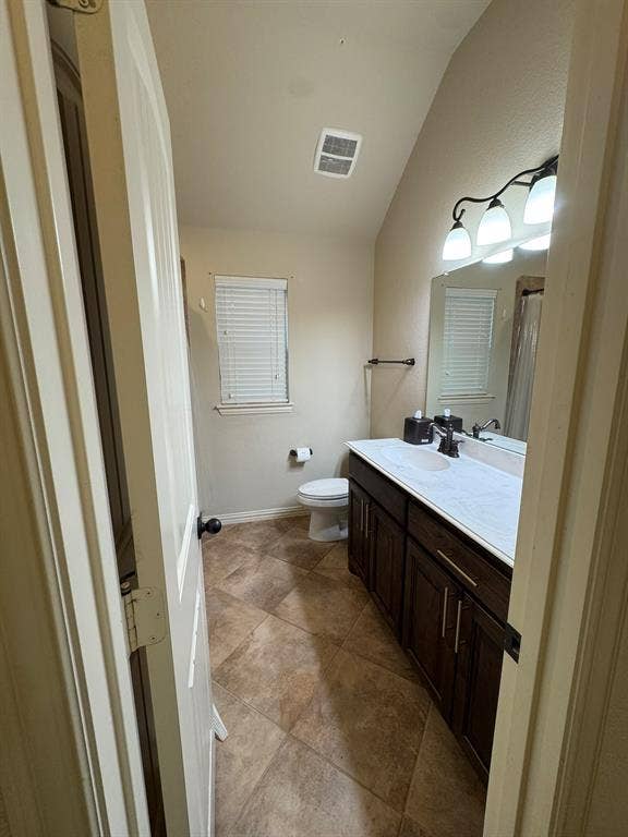 3953 Hollow Lake Road, Fort Worth, TX 76262 Dark wood-finish cabinetry featuring dual-basin vanity with a solid surface countertop, ceramic tile flooring, and vaulted ceiling