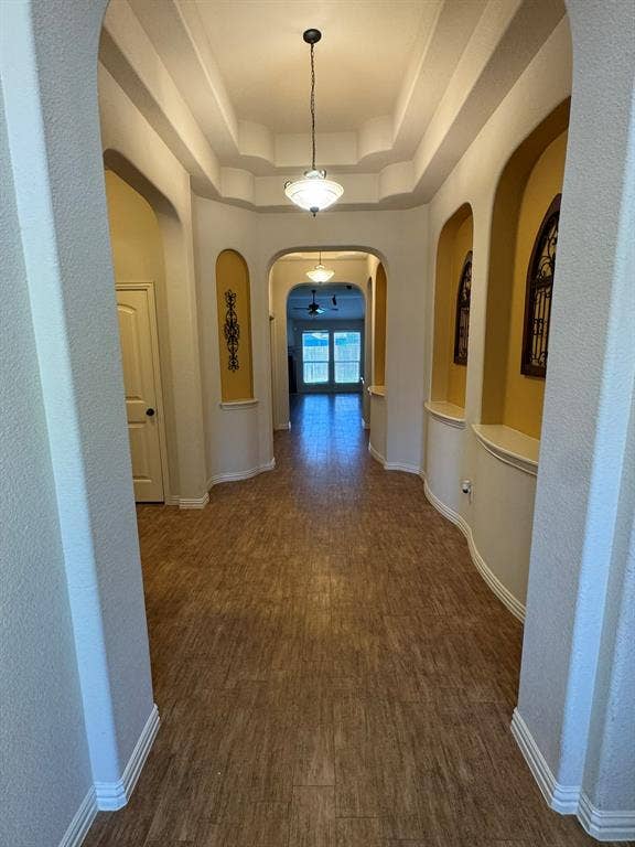 3953 Hollow Lake Road, Fort Worth, TX 76262 Hallway featuring arched architectural openings, built-in display niches, a tiered tray ceiling, pendant lighting, and wood-finish flooring