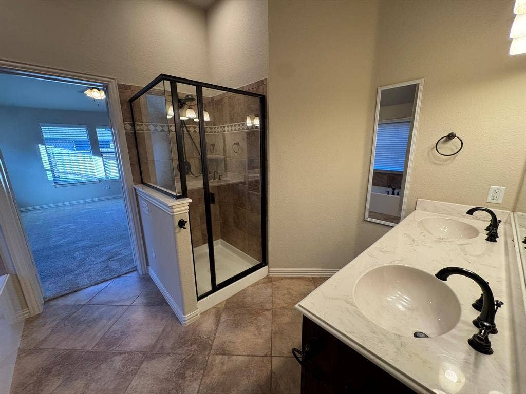 3953 Hollow Lake Road, Fort Worth, TX 76262 Bathroom featuring dual-sink vanity with stone-finish countertop, dark metal fixtures, tiled flooring, and a walk-in shower with a black-frame enclosure