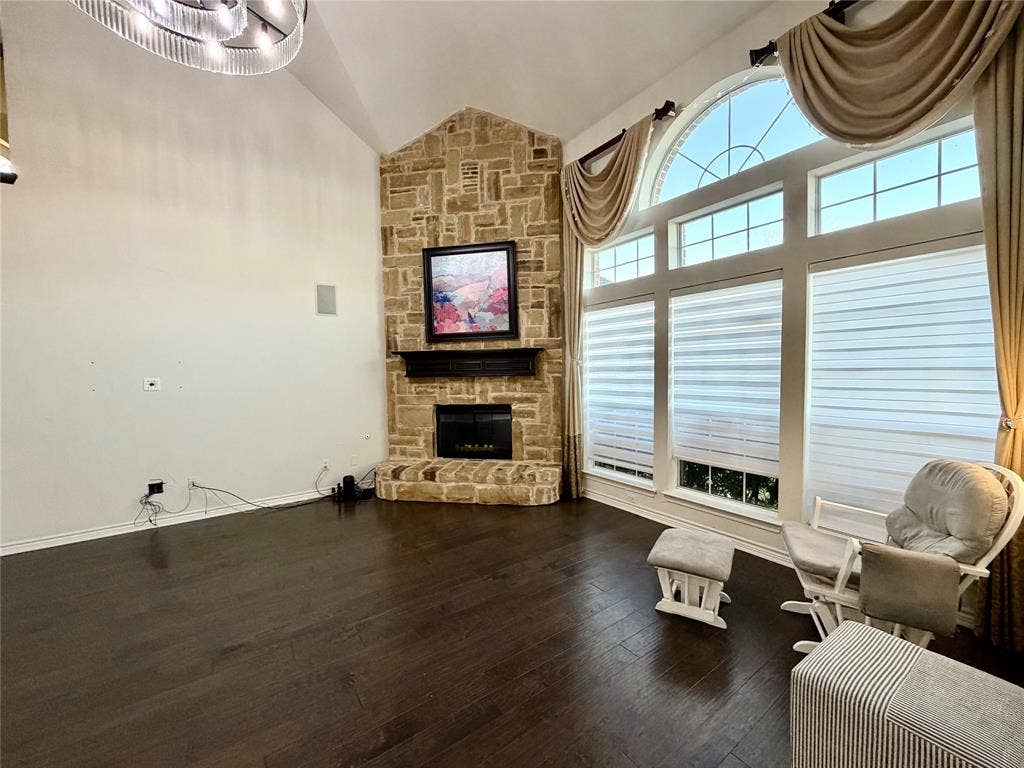 4514 Sea Sparrow Lane, Garland, TX 75043 Vaulted ceilings, floor-to-ceiling stone fireplace with a dark wood mantel, wood-finish flooring, and a multi-pane arched window ensemble