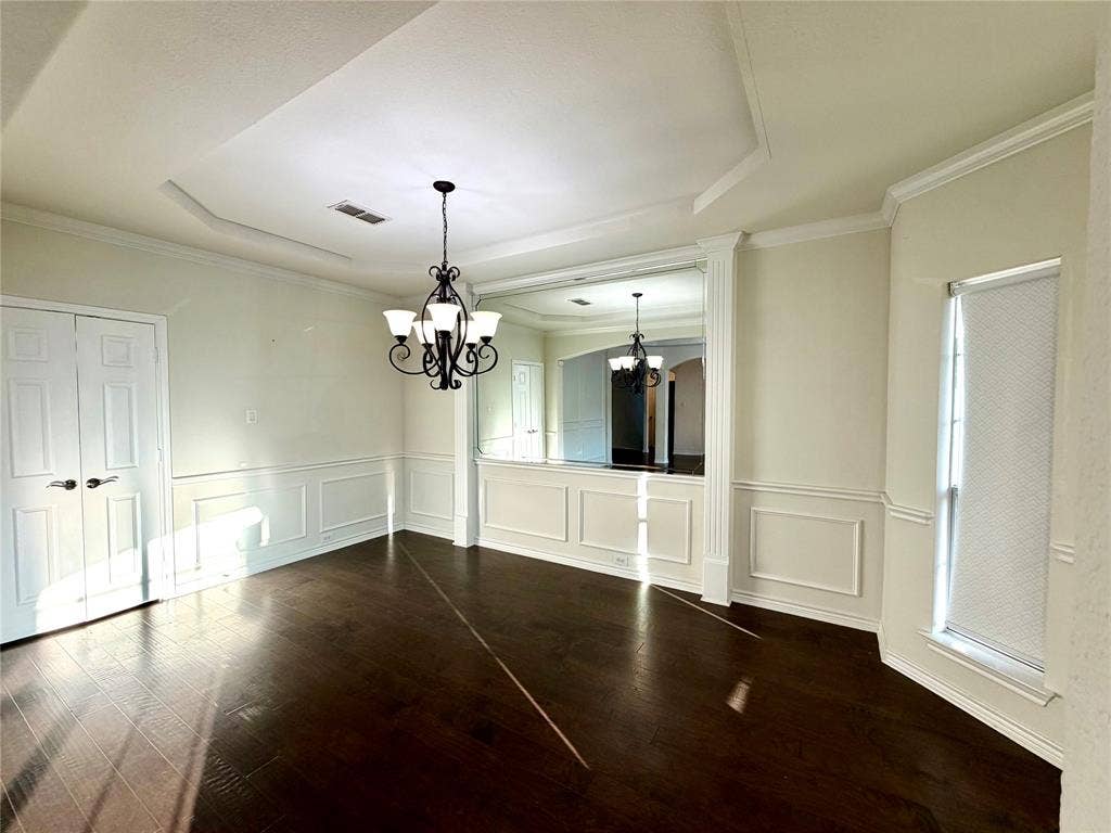 4514 Sea Sparrow Lane, Garland, TX 75043 Dining area featuring dark wood-finish flooring, recessed tray ceiling, custom wainscoting, integrated wall mirror, and a multi-light decorative chandelier