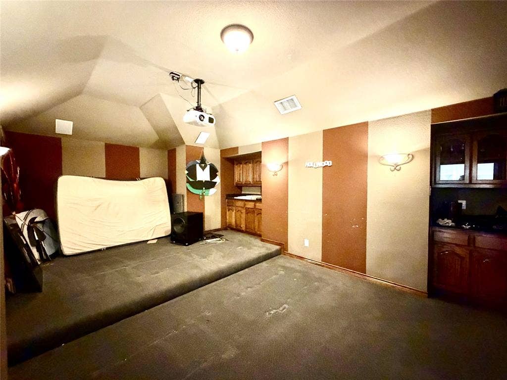 4514 Sea Sparrow Lane, Garland, TX 75043 Vaulted ceilings with mounted projector, tiered carpeted flooring, and built-in wood cabinetry with stone countertops