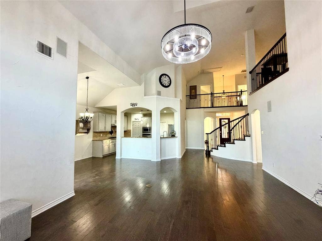 4514 Sea Sparrow Lane, Garland, TX 75043 Double-height ceiling with a modern drum chandelier, dark wood-finish flooring, staircase with a black metal balustrade, and arched architectural wall detailing