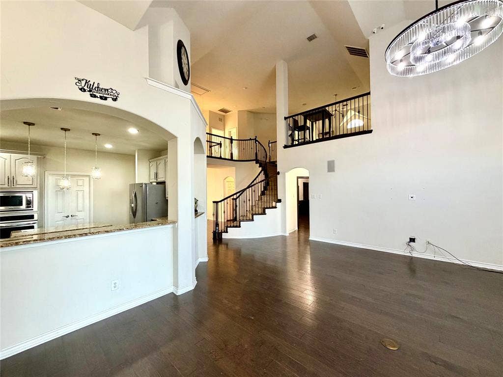 4514 Sea Sparrow Lane, Garland, TX 75043 Interior featuring high ceilings, wood-finish flooring, a curved staircase with wrought-iron railings, a mezzanine landing, and a contemporary oval-shaped pendant light fixture