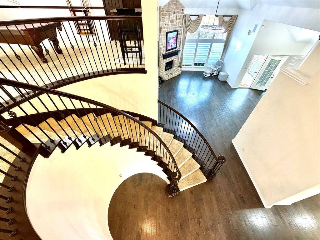 4514 Sea Sparrow Lane, Garland, TX 75043 Curved staircase featuring wood handrails and metal balusters, soaring vaulted ceilings, stone-clad fireplace, wood-finish flooring, and multi-pane windows
