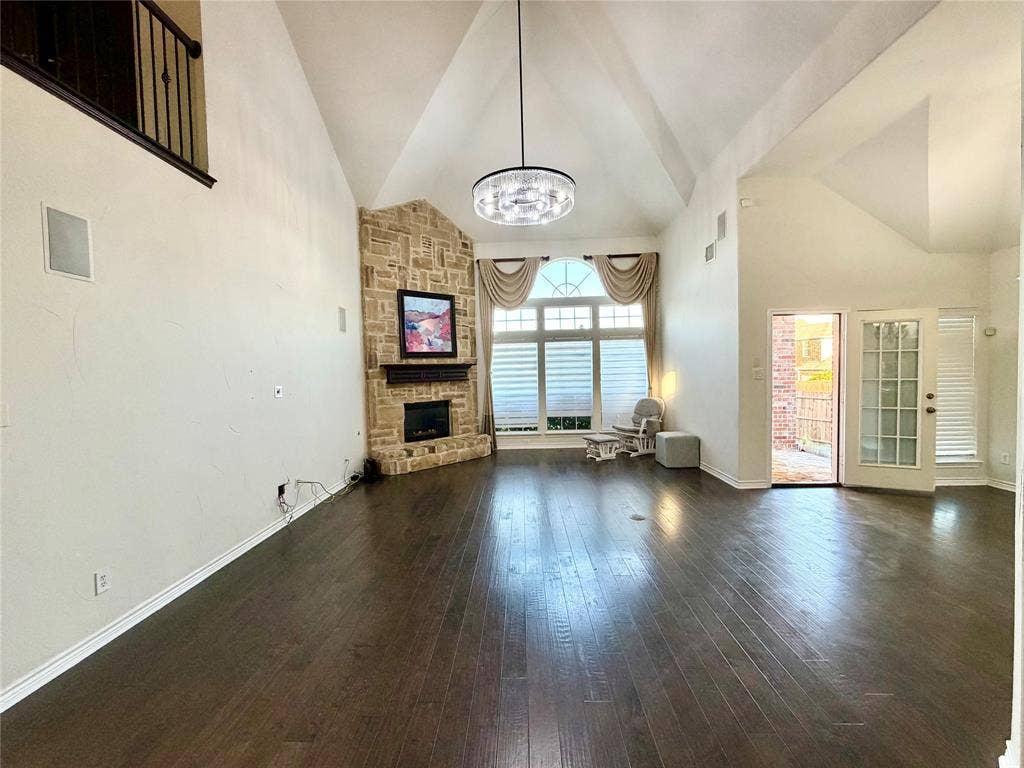 4514 Sea Sparrow Lane, Garland, TX 75043 Vaulted ceiling featuring a stone-clad fireplace, dark wood-finish flooring, large multi-pane windows, and a suspended circular chandelier