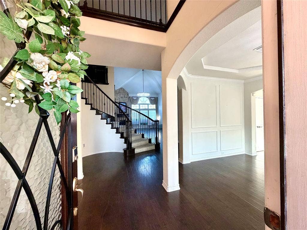 4514 Sea Sparrow Lane, Garland, TX 75043 Foyer entrance featuring wood-finish flooring, a two-story ceiling, a wrought-iron staircase railing, arched wall detailing, and a tray ceiling