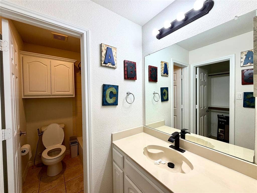 4514 Sea Sparrow Lane, Garland, TX 75043 Vanity featuring a solid surface countertop with an integrated basin, matte black faucet, full-width mirror, wall-mounted light fixture, and white cabinetry